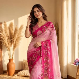 May include: A pink ombre saree featuring a deep magenta scalloped border with intricate floral embroidery. The garment includes a matching short-sleeved blouse with a V-neckline and detailed embroidery along the edges and sleeves.