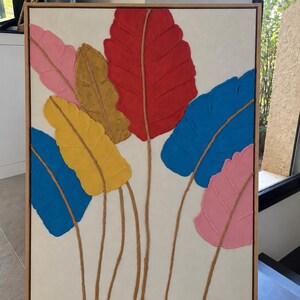 Peut inclure: Une œuvre d'art murale rectangulaire dans un cadre en bois clair présentant des formes de feuilles texturées et en relief en rose, doré, jaune, rouge et bleu sur fond blanc. Chaque feuille a une tige brune. La signature Chloé Anastasia est visible.