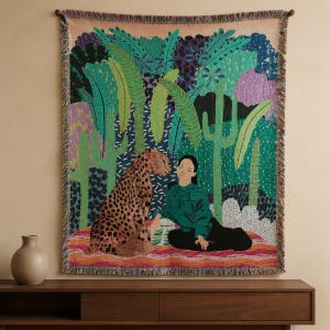 Peut inclure: Une tapisserie murale tissée représentant une scène de jungle colorée avec un léopard et une personne assis ensemble. Le motif inclut des feuilles de palmier vertes, des cactus et des accents violets. Le textile rectangulaire a des bords frangés.