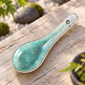 Peut inclure: Une cuillère à soupe en céramique avec un vernis brillant moucheté turquoise et blanc. La cuillère présente un bol large et arrondi ainsi qu'un long manche plat doté d'un petit trou circulaire à l'extrémité pour la suspendre.