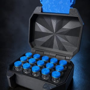 Peut inclure: Un étui de rangement noir au couvercle géométrique avec un loquet bleu vif, contenant quinze petits flacons en verre à bouchons bleus disposés en grille. L'étui présente une finition texturée et un couvercle articulé ouvert sur les flacons.