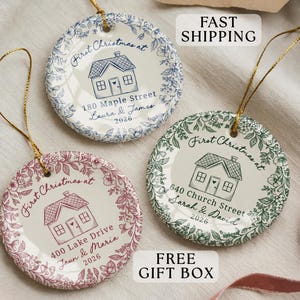 May include: Three round ceramic ornaments with gold hanging strings. Each features a house illustration, floral border, and text: First Christmas at, street address, names, and 2026. One is blue, one is pink, and one is green with white backgrounds.
