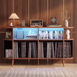 May include: A mid-century style wooden media console with rounded edges, featuring an open top shelf with blue LED lighting, two upper storage sections, and four lower compartments filled with vinyl records, books, and various decorative items.