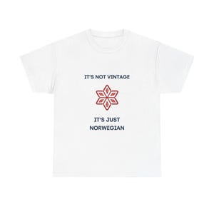 May include: A white short-sleeved t-shirt featuring the dark blue text IT'S NOT VINTAGE above a red six-pointed geometric star design, followed by the dark blue text IT'S JUST NORWEGIAN centred on the front of the garment.