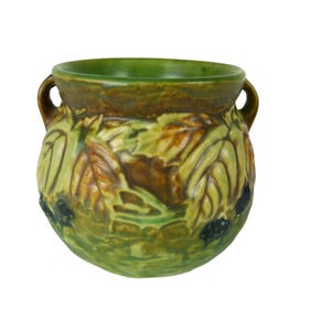 May include: A ceramic vase with a green interior and exterior, featuring a relief design of leaves and berries. The vase has two small handles and a rounded shape. The color palette includes shades of green, brown, and yellow.
