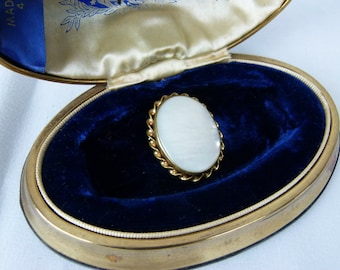 May include: A white oval-shaped cameo ring with a gold setting and a beaded border. The ring is displayed in a blue velvet-lined oval-shaped box.