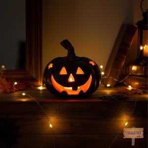 May include: A black ceramic jack-o'-lantern pumpkin with a carved face featuring triangular eyes, a nose, and a wide, toothy grin. The pumpkin has star-shaped cutouts on its upper surface and emits a warm, glowing orange light from within.