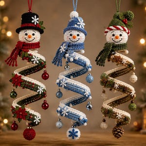 May include: Three crocheted snowman ornaments with spiral bodies. The left snowman wears a black hat and red scarf, the centre a blue hat and scarf, and the right a green hat and scarf. Each features snowflake accents and hanging baubles.