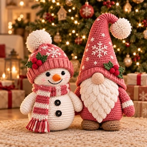Puede incluir: Un muñeco de nieve y un gnomo de ganchillo colocados uno al lado del otro. El muñeco de nieve lleva un gorro rosa con un pompón blanco, una bufanda a juego y dos botones negros. El gnomo lleva un gorro rosa alto con un copo de nieve.