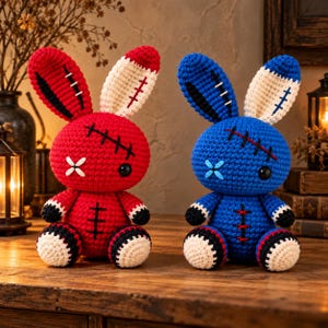 Puede incluir: Dos muñecos de conejo de peluche tejidos a ganchillo, uno rojo y otro azul, con detalles cosidos en negro, ojos desiguales y orejas interiores de color crema. Cada muñeco tiene una cabeza redonda, un cuerpo pequeño y extremidades con detalles.