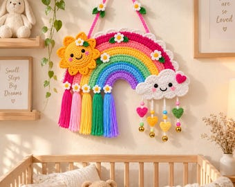 May include: A crocheted wall hanging featuring a vibrant rainbow with a yellow sun on the left and a white cloud on the right. The rainbow is decorated with small white flowers and colorful yarn tassels. The cloud has dangling heart charms.