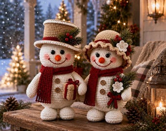 May include: Two crocheted snowmen figures standing on a wooden surface. The left snowman wears a tan top hat with holly, while the right snowman wears a tan bonnet with white flowers. Both have red scarves, orange noses, and brown buttons.