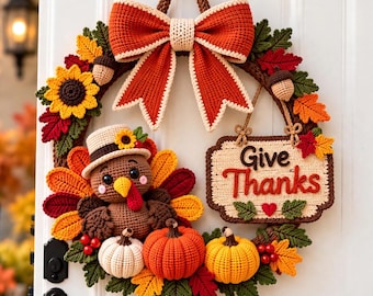 May include: A crochet wreath featuring a large orange bow at the top, a turkey wearing a hat, three small pumpkins, sunflowers, acorns, and autumn leaves. A rectangular sign hangs from the wreath with the text Give Thanks in brown and red.