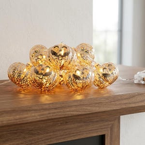 May include: A string of decorative lights featuring spherical, mercury glass-style bulbs with a warm, metallic gold finish. The bulbs are connected by a thin, clear wire and include a rectangular white battery pack for power operation.