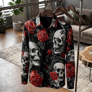 May include: A long-sleeve button-down shirt in black featuring a repeating pattern of realistic human skulls and vibrant red roses. The shirt has a standard collar, buttoned cuffs, and a full-length front button placket, displayed on a wooden hanger.