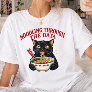 Könnte beinhalten: Ein weißes kurzärmeliges T-Shirt mit einer Grafik eines schwarzen Katers, der eine Schüssel Ramen mit roten Stäbchen isst. Der Text über dem Kater lautet "NOODLING THROUGH THE DATA" in roten Großbuchstaben. Das Shirt hat einen Rundhalsausschnitt.