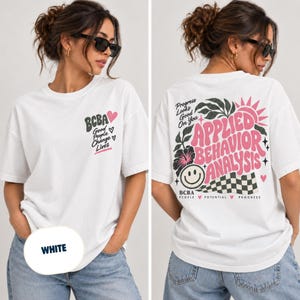 Könnte beinhalten: Ein weißes T-Shirt mit einer kleinen Grafik auf der Vorderseite mit dem Text BCBA Good People Change Lives und Herzen. Die Rückseite zeigt eine große Grafik mit dem Text Applied Behavior Analysis, Progress Looks Good On You und BCBA People Potential Progress, zusammen mit einem Smiley, einem Schachbrettmuster und floralen Elementen.