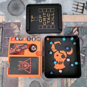 Può includere: Un set organizer per giochi da tavolo in plastica nera e arancione con un coperchio che riporta il testo TP, CP, CRIT, TAC, KILL. Il vassoio include scomparti per gettoni, carte e un'area per tirare i dadi con un teschio e vari dadi.