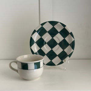 Peut inclure: Une tasse à thé et une soucoupe en céramique blanche avec un motif à carreaux noirs et verts. La soucoupe a un motif à carreaux plus grand que la tasse à thé.