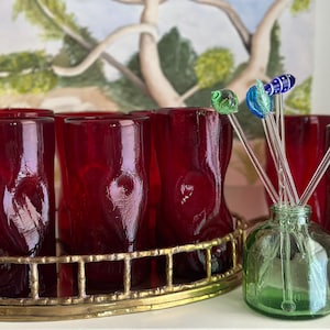 Może przedstawiać: Sześć czerwonych szklanek z tacą z mosiądzu i zieloną szklaną butelką z pięcioma szklanymi mieszadłami z kolorowymi szklanymi koralikami na końcach.