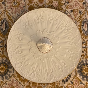 Può includere: Piatto da portata in ceramica bianca con bordo dorato e design decorato. Il piatto ha una maniglia centrale con un accento rosso.