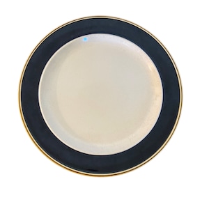 May include: A white ceramic plate with a black rim and a gold trim. The plate is empty.