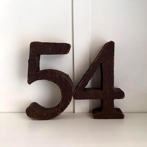 May include: Two brown, textured numbers, 5 and 4, stand side-by-side against a white background. The numbers are made of a rough material, possibly wood or cardboard, and have a rustic appearance. The number 5 is slightly taller than the number 4.