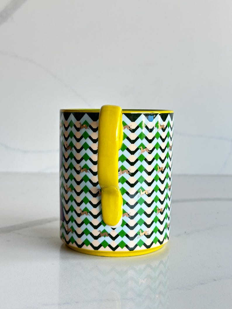 Op de afbeelding: Een witte keramische mok met een zwarte handgreep en de tekst "But First, Coffee" in een vetgedrukte, zwarte letter. De mok staat tegen een vage achtergrond, wat een gezellige setting suggereert.