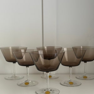May include: Set of six brown glass champagne coupes. The glasses have a wide, shallow bowl and a long, thin stem.
