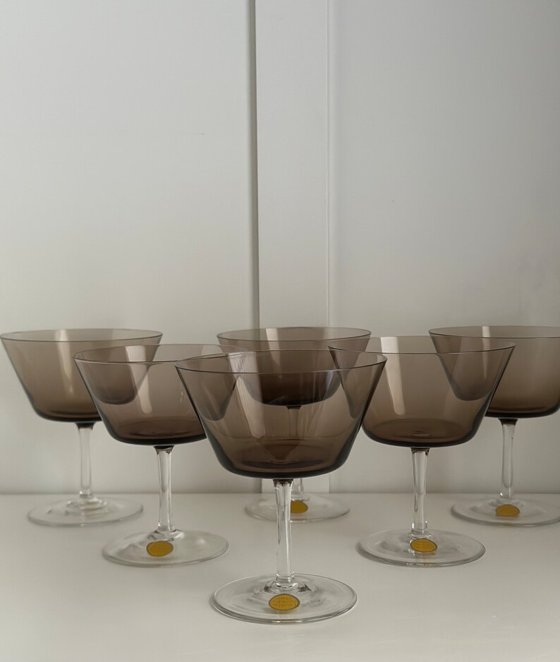 May include: Set of six brown glass champagne coupes. The glasses have a wide, shallow bowl and a long, thin stem.