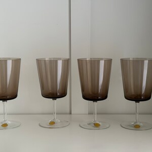 May include: Four clear glass wine glasses with a brown tint. The glasses are arranged in a row on a white surface.