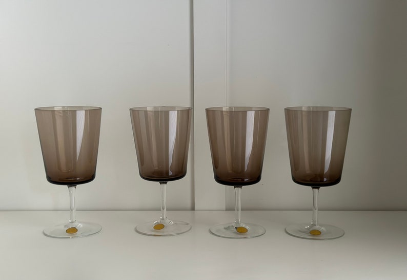 May include: Four clear glass wine glasses with a brown tint. The glasses are arranged in a row on a white surface.