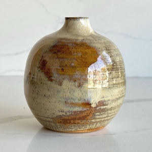 May include: A spherical ceramic vase with a narrow neck and a glossy finish. The surface features a blend of earthy beige, cream, and deep amber brown tones with visible horizontal texture lines and a mottled, organic glaze pattern throughout.