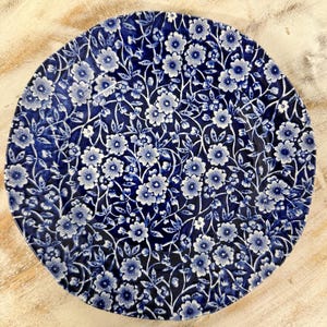 Puede incluir: Un plato de cena con estampado floral azul y blanco. El plato tiene un fondo blanco con un estampado floral azul.