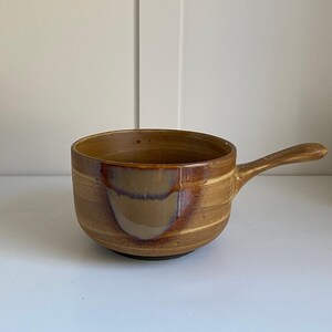 May include: A brown ceramic bowl with a handle. The bowl has a mottled glaze with brown, orange, and white streaks.