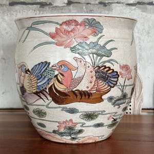 Könnte beinhalten: Ein weißer Keramiktopf mit floralem und Vogelmotiv. Der Topf zeigt rosa und grüne Lotusblumen, blaue und grüne Blätter und zwei mehrfarbige Vögel.