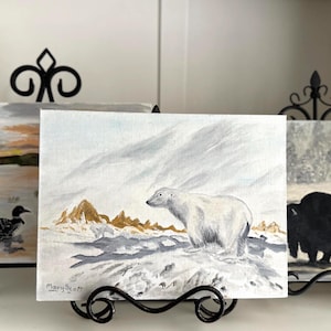 Könnte beinhalten: Ein Gemälde eines Eisbären in einer verschneiten Landschaft. Der Bär ist weiß mit einem grauen Schatten, vor einem Hintergrund aus Schnee und Bergen. Das Gemälde ist mit "Mary Scott" signiert.
