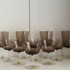 May include: Set of eight brown glass stemmed drinking glasses. Six of the glasses are smaller and have a wider bowl, while two are taller and narrower.