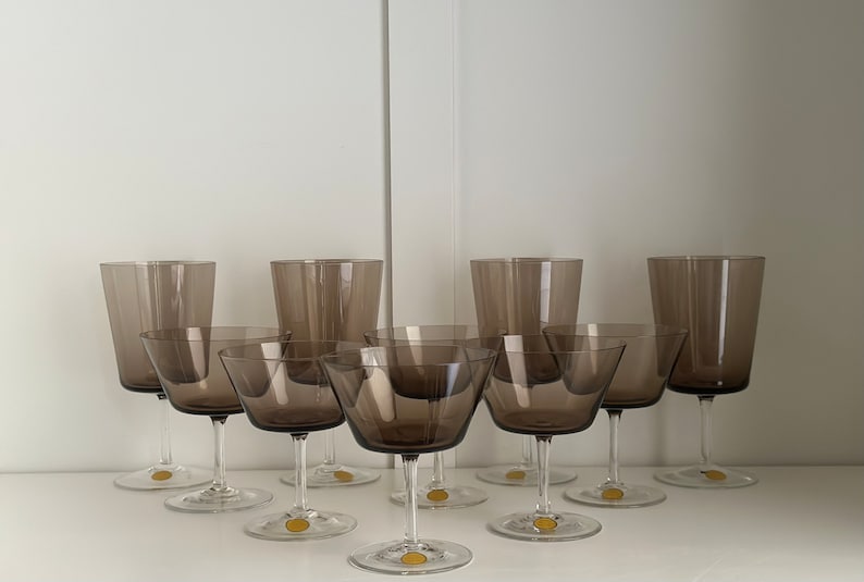 May include: Set of eight brown glass stemmed drinking glasses. Six of the glasses are smaller and have a wider bowl, while two are taller and narrower.