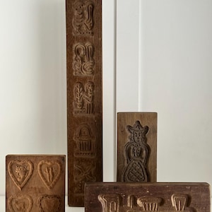 Puede incluir: Conjunto de cinco cortadores de galletas de madera vintage. Los cortadores presentan varios diseños, incluyendo un tren, una mujer, un corazón y un pájaro. Los cortadores están hechos de madera marrón oscura y tienen un aspecto rústico.