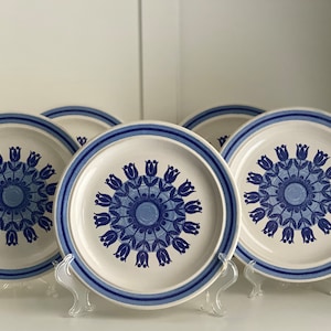 Pode incluir: Quatro pratos de jantar de cerâmica azul e branca com um design floral. Os pratos têm uma borda azul e um centro branco com um padrão floral azul.