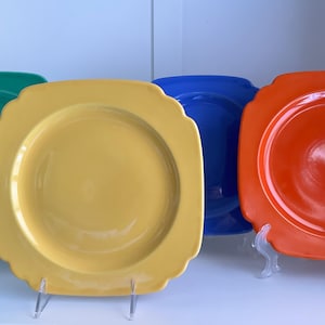 Puede incluir: Cuatro platos cuadrados de cerámica en diferentes colores: verde, amarillo, azul y naranja. Los platos tienen un borde ligeramente elevado y un borde festoneado.