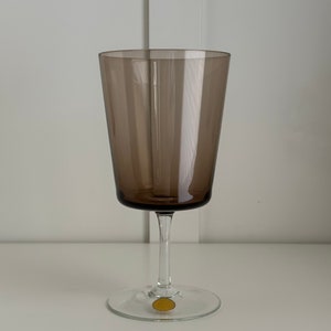 May include: A dark brown glass wine glass with a clear stem and base. The base has a gold sticker with the text "Cristal d'Arques" on it.
