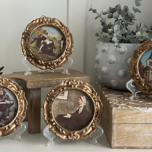 Puede incluir: Cuatro marcos de fotos adornados en tono dorado con varias imágenes en su interior, expuestos en un estante de madera con una maceta gris y una caja de madera.