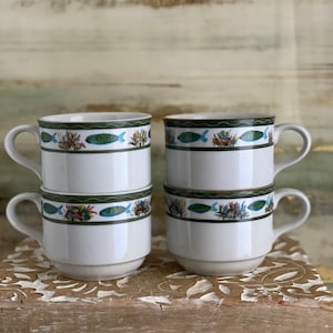 May include: Set of four white ceramic mugs with a green, blue, and white fish and coral design. The mugs are stacked on top of each other.