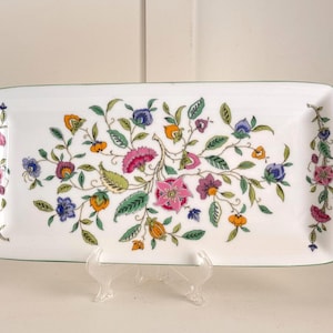 May include: Rectangular white serving platter with a floral design. The platter features a central arrangement of pink, purple, orange, and blue flowers with green leaves. The edges are trimmed with a green border.
