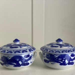 Op de afbeelding: Twee kleine blauwe en witte porseleinen kommen met deksels. De kommen hebben een drakenontwerp en zijn perfect om kleine porties voedsel te serveren.