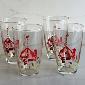 May include: Four clear drinking glasses with a red barn and animal design. Each glass features a red barn with a white horse and cow illustration. The glasses are cylindrical and suitable for various beverages.