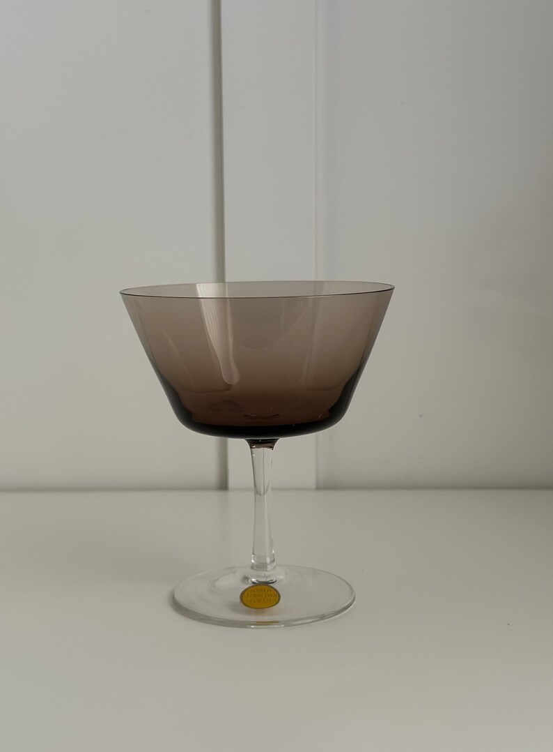 May include: A clear glass stemmed goblet with a brown tinted bowl. The goblet has a gold sticker on the bottom with the text "Made in Czechoslovakia".