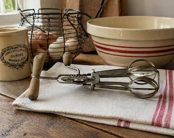 Batidora de huevos manual con manivela y mango de madera.